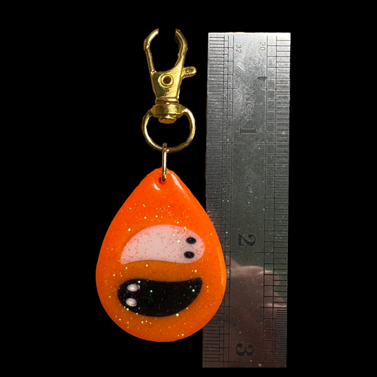Resin Charm - 2 Ghosts float on a Sparkly Orange Background that Glows in the Dark